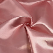 A close-up of draped satin fabric in a soft dusty pink color, showing its smooth texture and sheen.