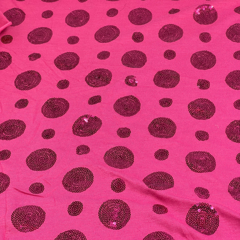 Bright pink fabric with scattered dark magenta sequined polka dots of varying sizes.