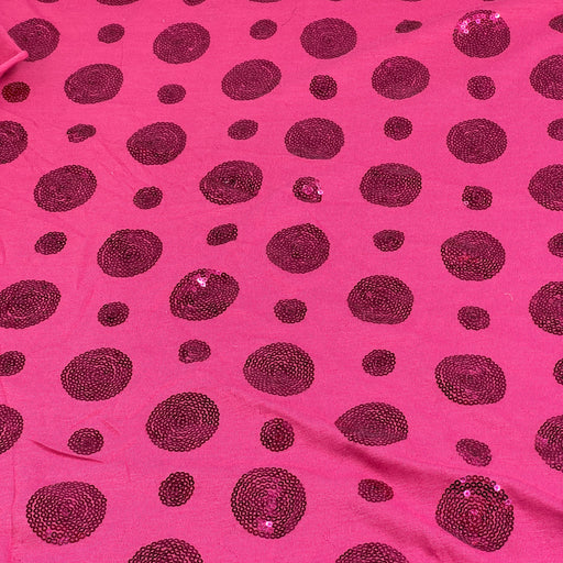 Bright pink fabric with scattered dark magenta sequined polka dots of varying sizes.