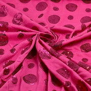 Pink sequined fabric with a pattern of dark magenta sequin spots, draped in a swirl to show texture and pattern.