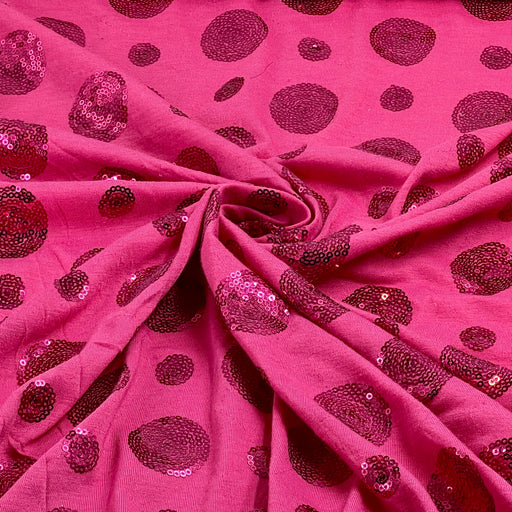 Pink sequined fabric with a pattern of dark magenta sequin spots, draped in a swirl to show texture and pattern.