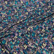 Purple floral fabric with a dense pattern of blue, teal, and cream flowers, draped diagonally across the frame.