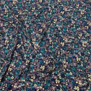 A close-up of a sheer purple mesh fabric with an all-over dense floral print in teal blue, yellow, and black.