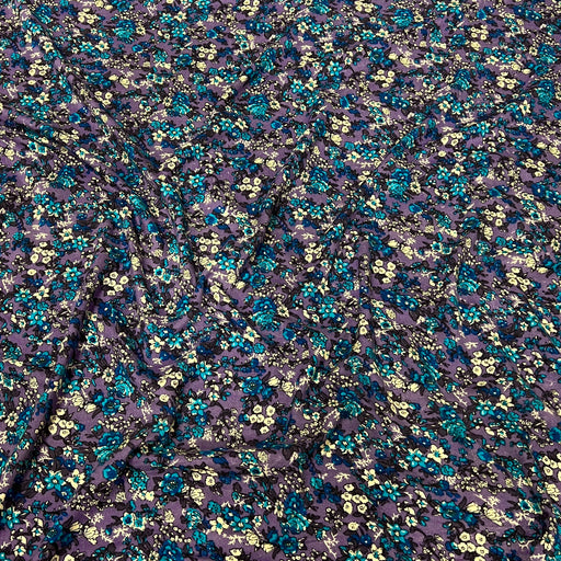 A close-up of a sheer purple mesh fabric with an all-over dense floral print in teal blue, yellow, and black.