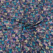 Purple floral fabric with a dense pattern of blue, teal, and cream flowers, gathered in the center to show its drape and texture.