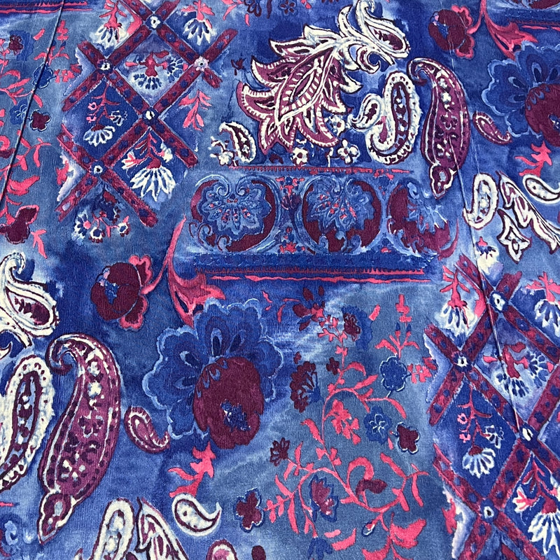 A close-up of a blue patterned fabric with intricate paisley and floral motifs in red, burgundy, cream, and white.
