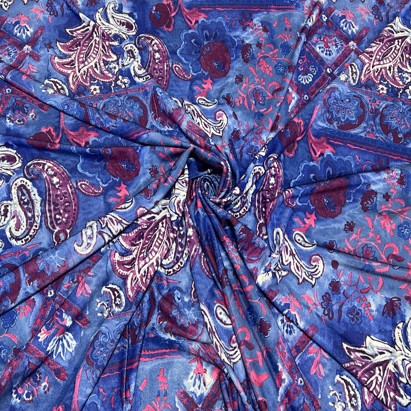 A close-up of a draped fabric with a blue paisley pattern featuring pink, burgundy, and white details.