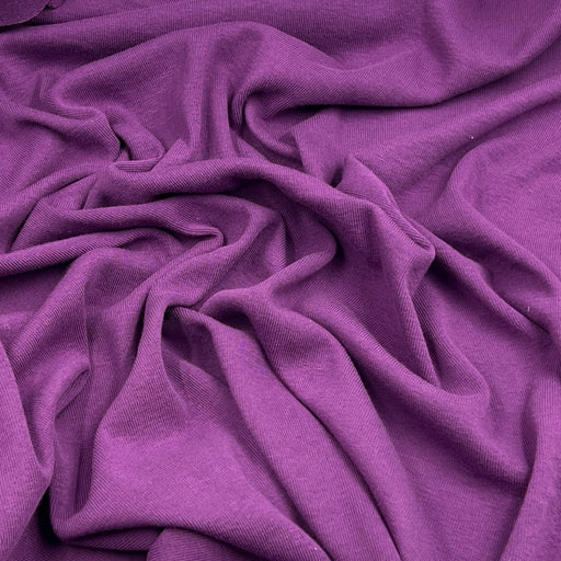 A close-up of draped purple fabric with soft folds and a smooth, slightly lustrous texture filling the frame.