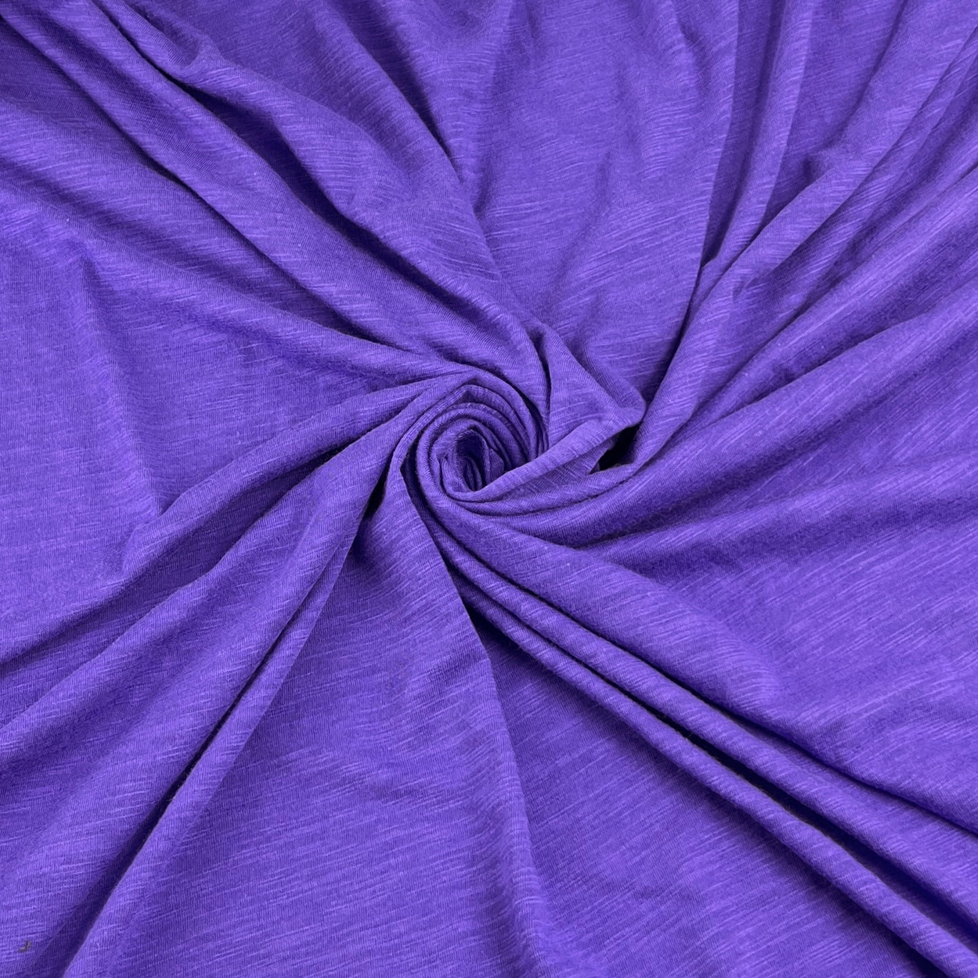 Purple heathered fabric draped in a spiral pattern, showing its soft texture and drape.