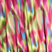 A close-up of a colorful abstract patterned fabric with flowing folds, featuring bright pink, lime green, blue, and yellow tones.