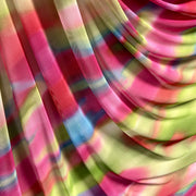 A close-up of draped sheer fabric with a multicolor tie-dye pattern in pink, lime green, blue, and yellow.