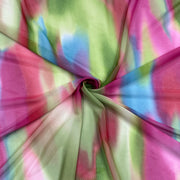 A close-up of a sheer fabric draped in a spiral, showing a tie-dye pattern with pink, green, blue, and white colors.