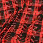 Red and black plaid fabric with a classic tartan pattern, shown draped to display its texture and folds.