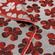 A close-up of a woven fabric with a red and white floral pattern, folded over to show the texture and red stitched edge.