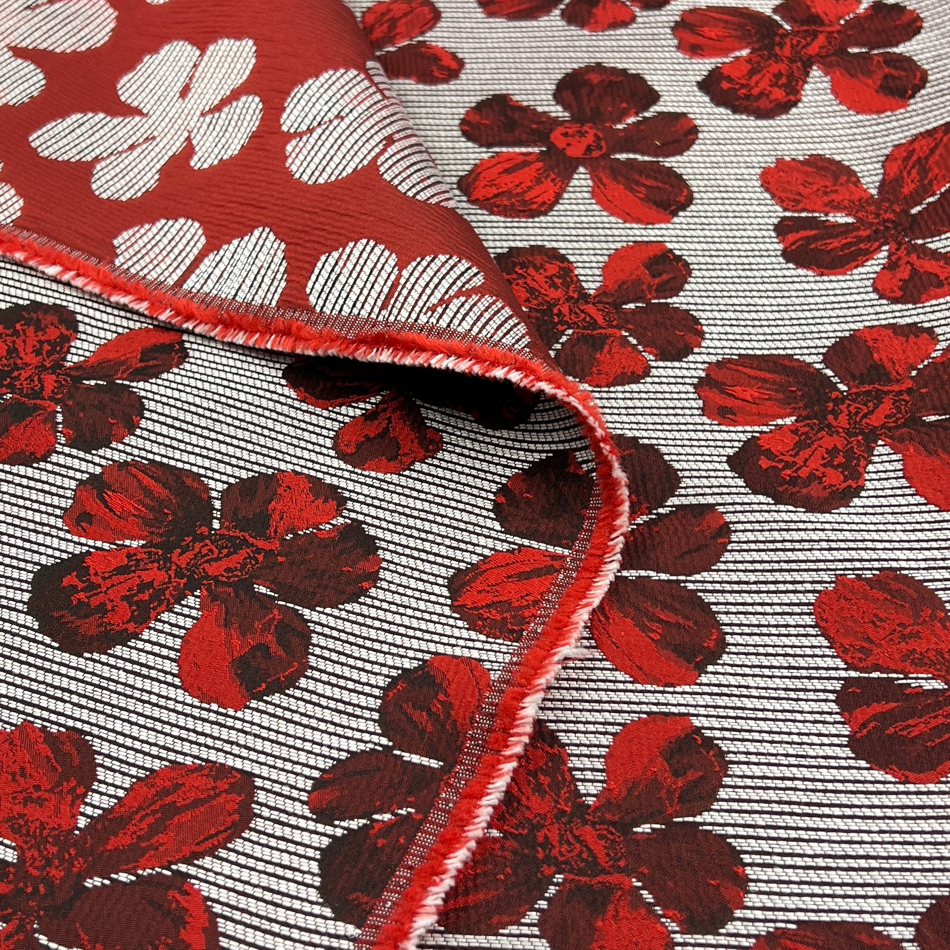 A close-up of a woven fabric with a red and white floral pattern, folded over to show the texture and red stitched edge.