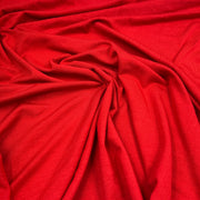 A close-up of bright red fabric with soft folds and a smooth, slightly lustrous texture filling the frame.