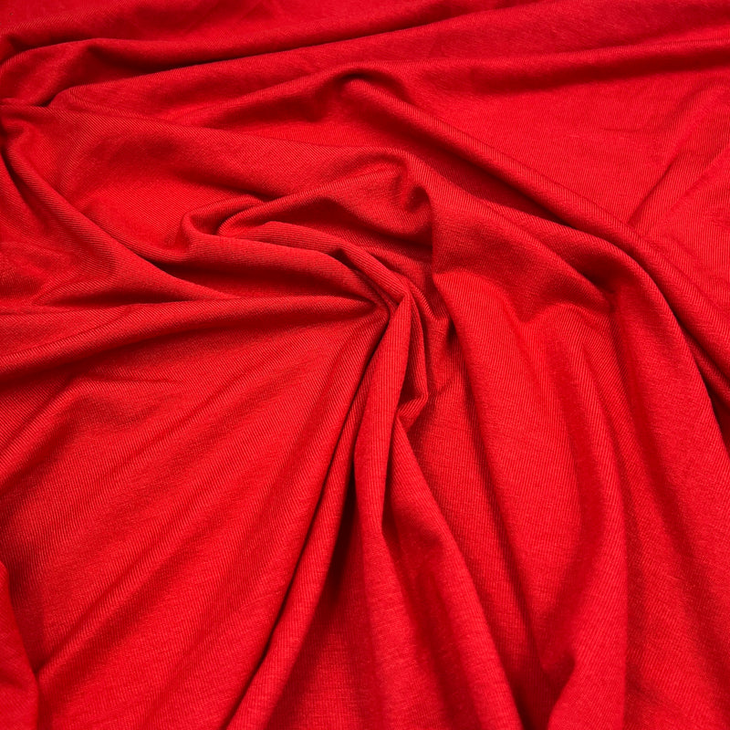 A close-up of bright red fabric with soft folds and a smooth, slightly lustrous texture filling the frame.