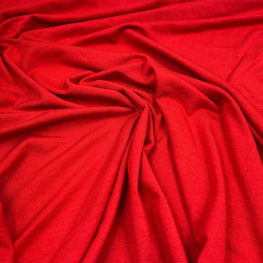 A close-up of bright red fabric with soft folds and a smooth, slightly lustrous texture filling the frame.
