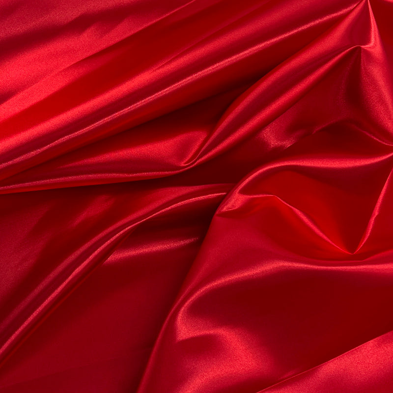 Red satin fabric draped in elegant folds, showcasing its smooth texture and glossy sheen.