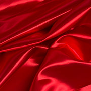 Red satin fabric with a glossy, lustrous sheen, draped in soft folds and creases.