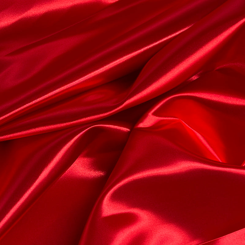 Red satin fabric with a glossy, lustrous sheen, draped in soft folds and creases.