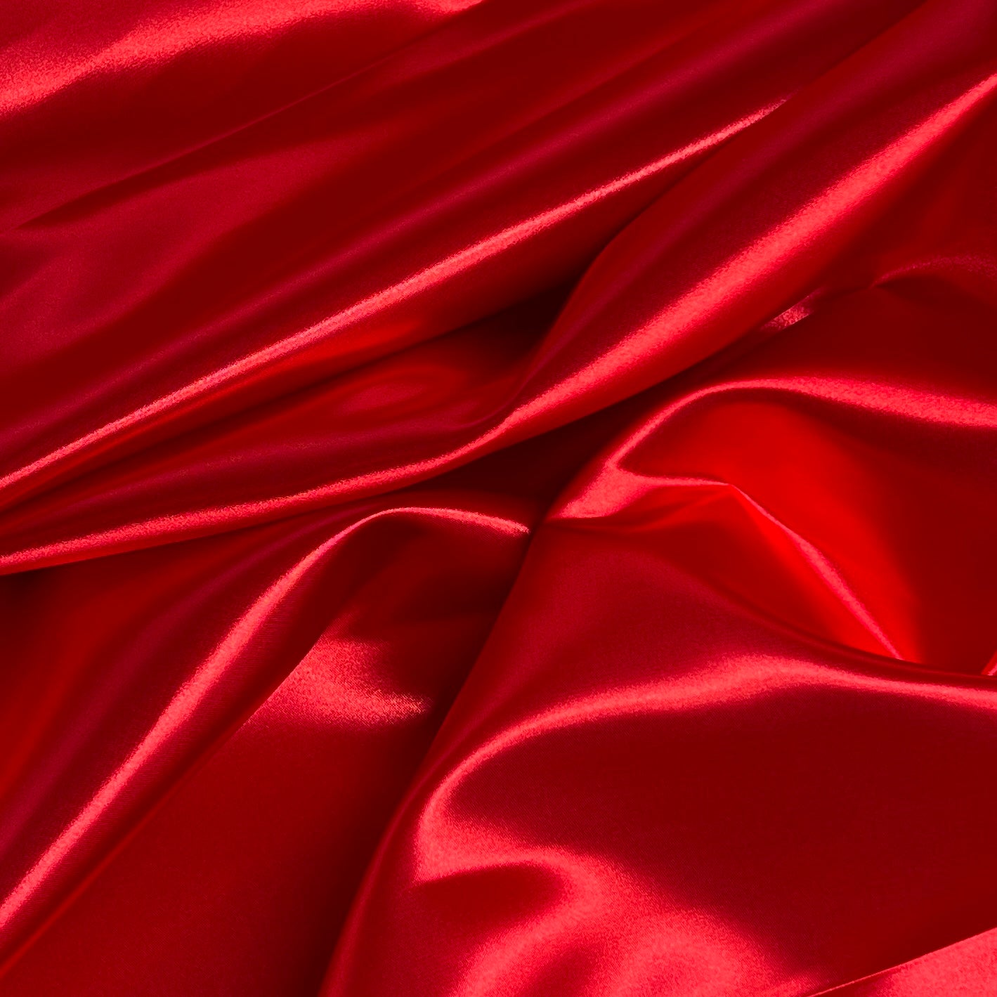 Red satin fabric with a glossy, lustrous sheen, draped in soft folds and creases.