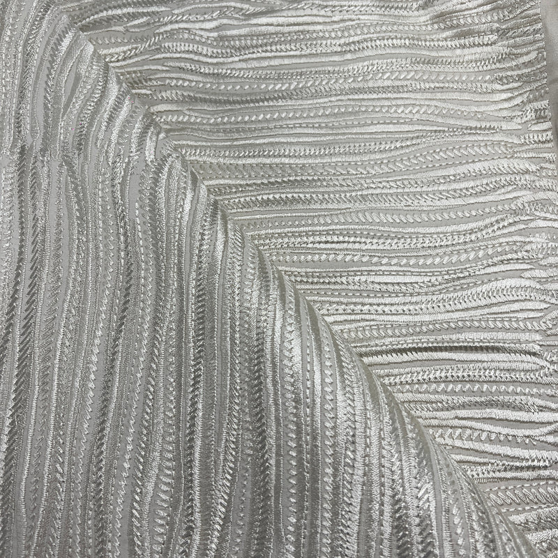 A close-up of a textured silver fabric with a raised, wavy chevron pattern.