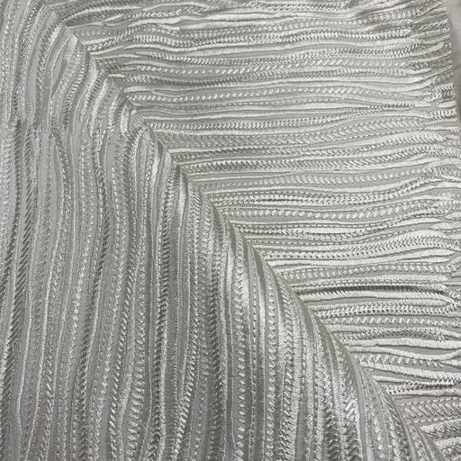 A close-up of a textured silver fabric with a raised, wavy chevron pattern.