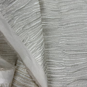 A close-up of textured fabric with horizontal wavy stripes in metallic silver and light gray, with a folded section showing the material's soft edge.