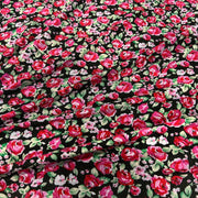 Black fabric with a dense floral print featuring red and pink roses, green leaves, and small white blossoms.