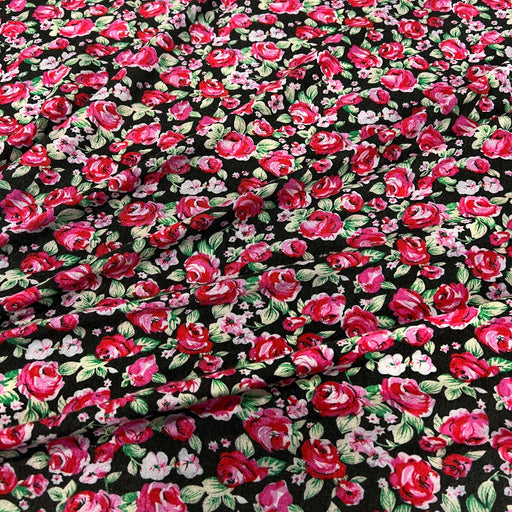 Black fabric with a dense floral print featuring red and pink roses, green leaves, and small white blossoms.