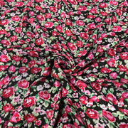 Black fabric with a dense red and pink floral print, featuring green leaves and light pink blossoms, styled with a central swirl.