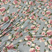 Light blue-gray floral fabric with a repeating print of pink and white roses, green leaves, and small yellow accents, shown draped with soft folds.