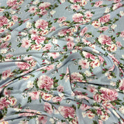 Light blue floral fabric with a repeating pattern of pink and white peonies with green leaves, draped to show its texture and print.