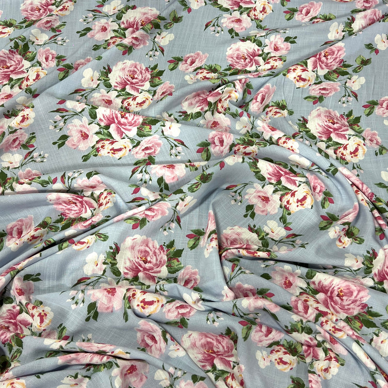 Light blue floral fabric with a repeating pattern of pink and white peonies with green leaves, draped to show its texture and print.