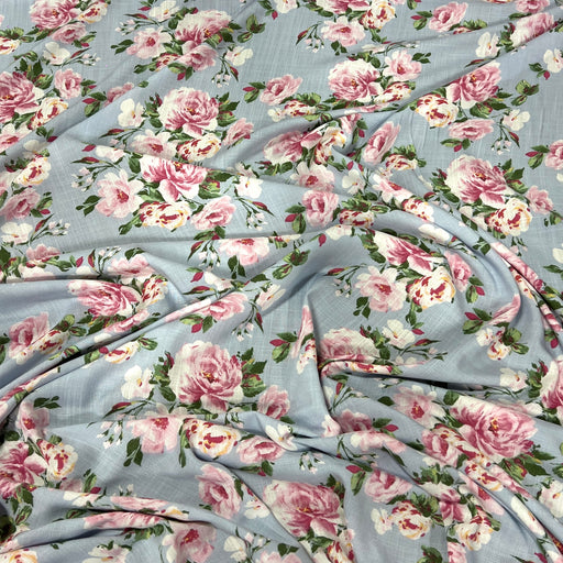 Light blue floral fabric with a repeating pattern of pink and white peonies with green leaves, draped to show its texture and print.