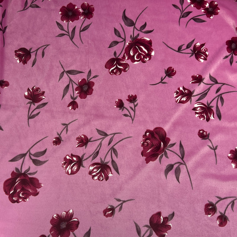 A close-up of a pink fabric with a repeating rose and leaf pattern in deep burgundy and silver.