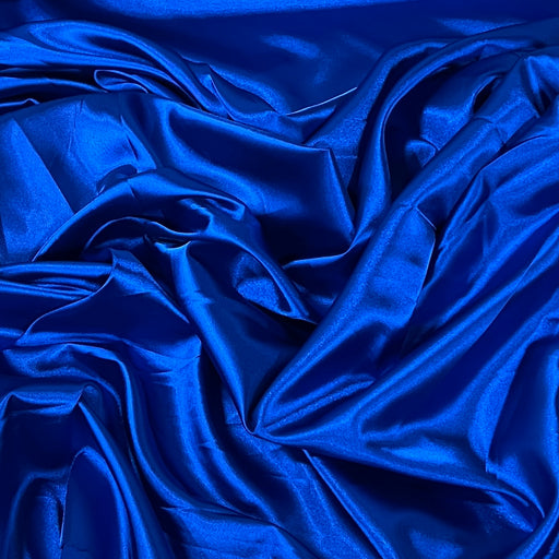 A close-up of draped royal blue satin fabric with soft folds and a glossy sheen.