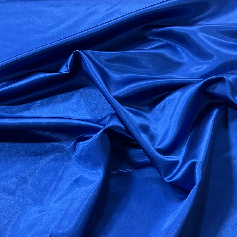 A close-up of draped royal blue satin fabric with soft folds and a glossy sheen.
