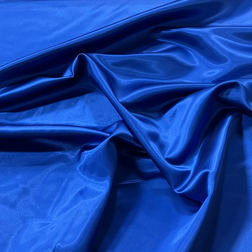 A close-up of draped royal blue satin fabric with soft folds and a glossy sheen.