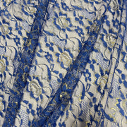 A close-up of a royal blue floral lace fabric with gold glitter accents over a white mesh background.