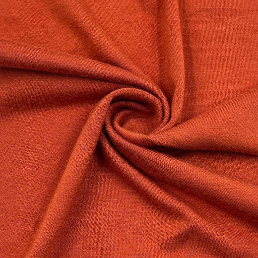 Closeup of rust orange rayon lycra jersey knit fabric pulled into a swirl showing soft hand and fluid drape. 