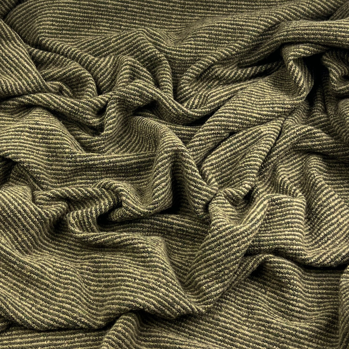 A close-up of a textured, olive green and beige striped knit fabric with a ribbed pattern, shown in soft folds.