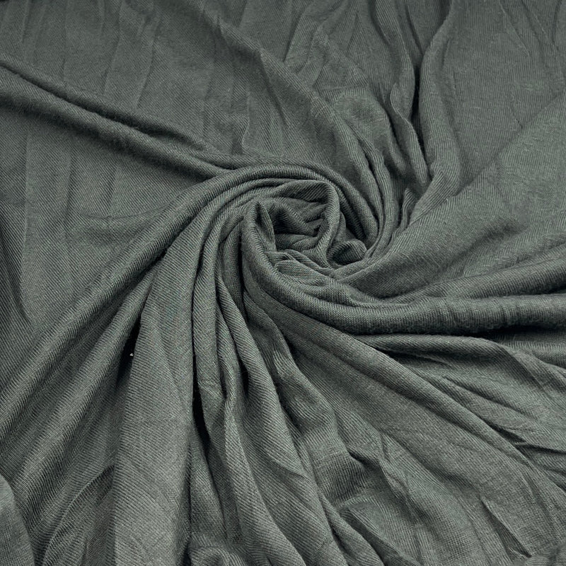 A close-up of draped fabric in a muted gray-green color, arranged in a spiral pattern to show texture and drape.