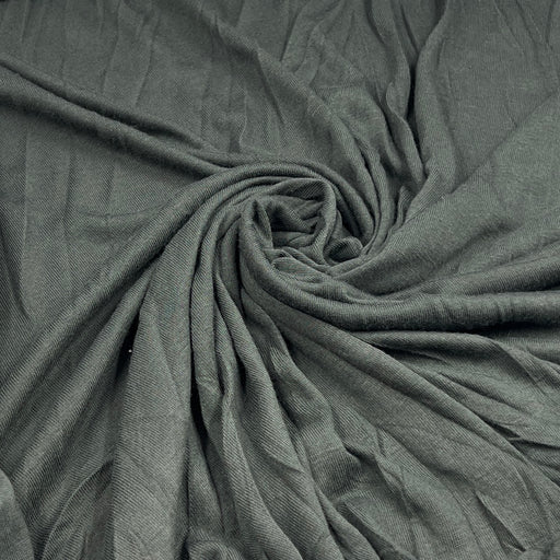 A close-up of draped fabric in a muted gray-green color, arranged in a spiral pattern to show texture and drape.