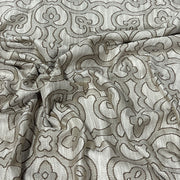 A close-up of draped fabric with an ornate repeating damask-style pattern in taupe and light beige.