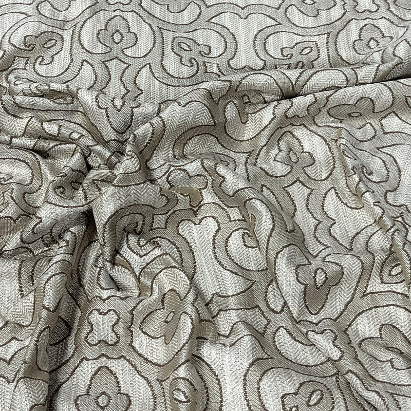 A close-up of draped fabric with an ornate repeating damask-style pattern in taupe and light beige.