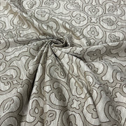 A close-up of draped fabric with an allover woven floral and scroll pattern in taupe and off-white.