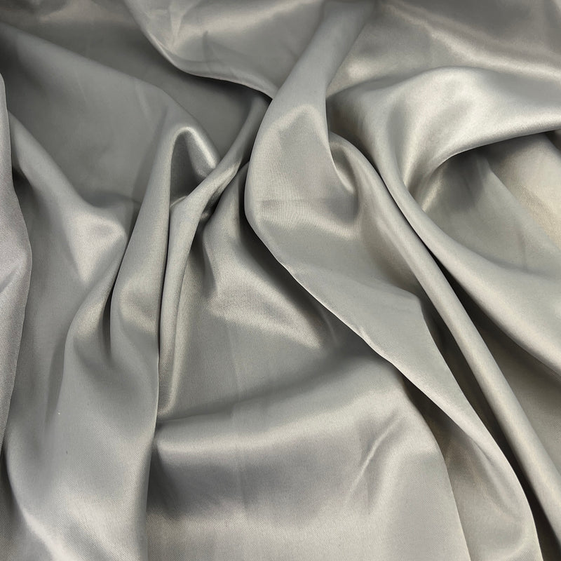 A close-up of draped satin fabric in a light silver-gray color, showing its smooth texture and sheen.
