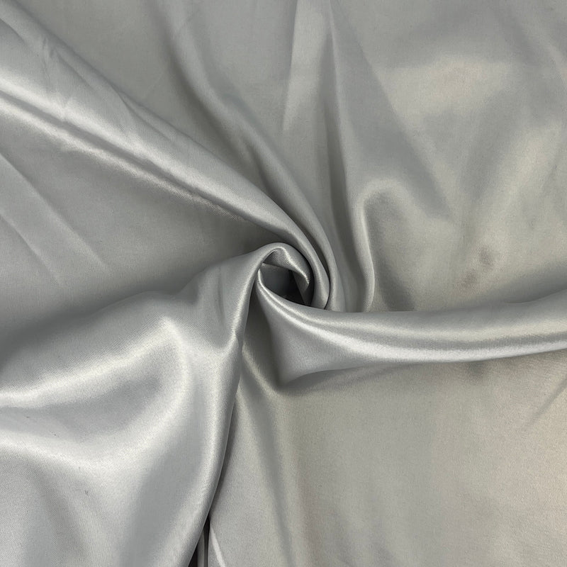 A close-up of draped satin fabric in a light silver-gray color, showing soft folds and a subtle sheen.
